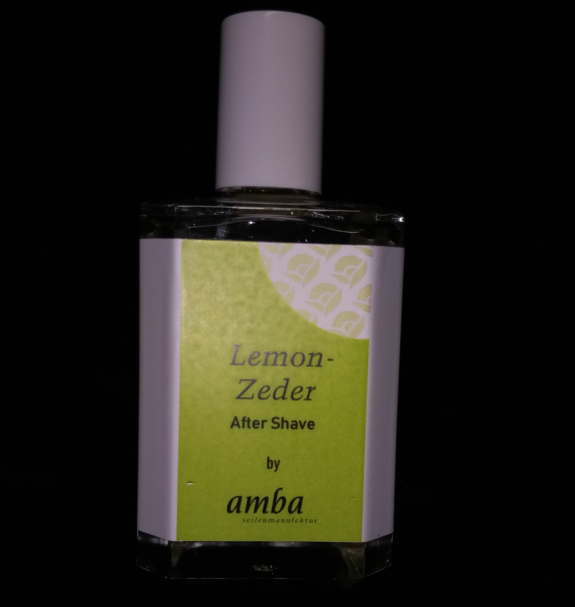 Ein viereckiger Glasflakon mit grünem Etikett auf dem Lemon Zeder After Shave by amba steht